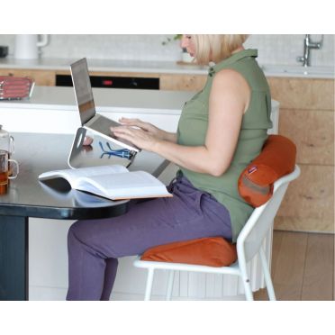 Kobieta pracuje przy komputerze, siedząc na krześle z małym wałkiem gryczanym WellB w kolorze terakoty za plecami jako podparcie.